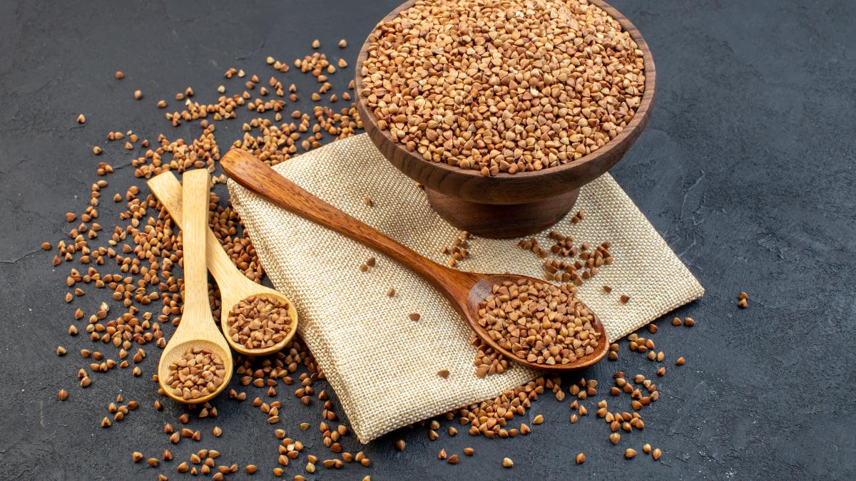 front-view-brown-buckwheat-inside-plate-with-pair-spoons-dark-background_44912500